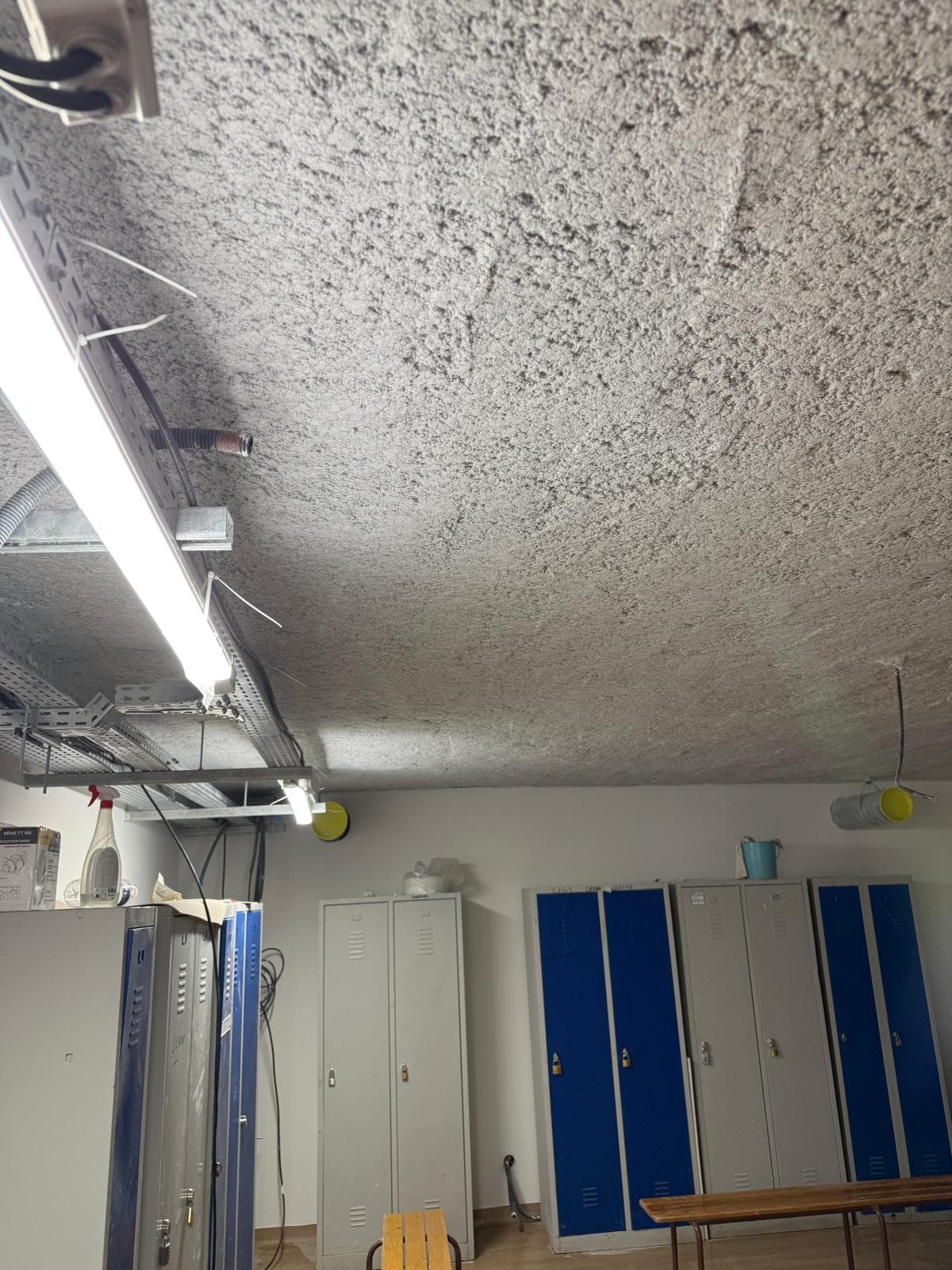 Protection incendie par flocage projeté au plafond dans la zone des vestiaires, démontrant l'adaptation aux bâtiments existants.