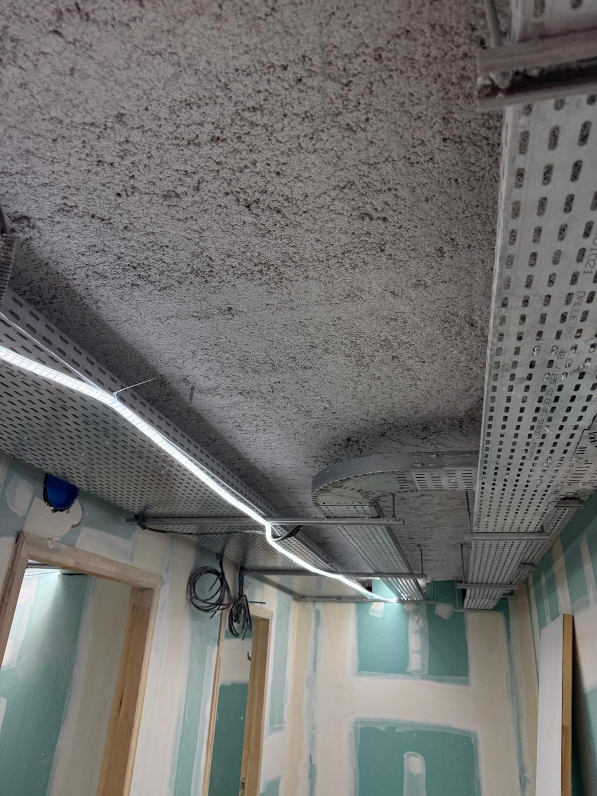 Flocage coupe-feu finalisé au plafond d'un couloir, intégrant parfaitement les chemins de câbles métalliques suspendus.